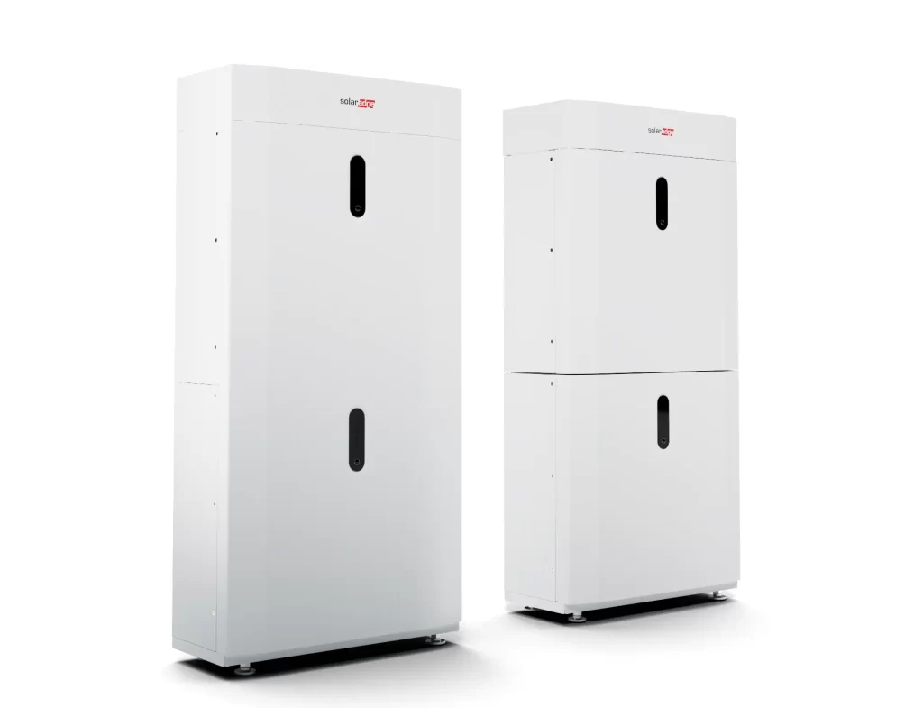 Two white, vertical battery storage units from SolarEdge Energy Bank. The unit on the left is a single-tower design, while the one on the right features two stacked sections. Both units have minimalist, sleek designs with a small black vertical strip in the center.