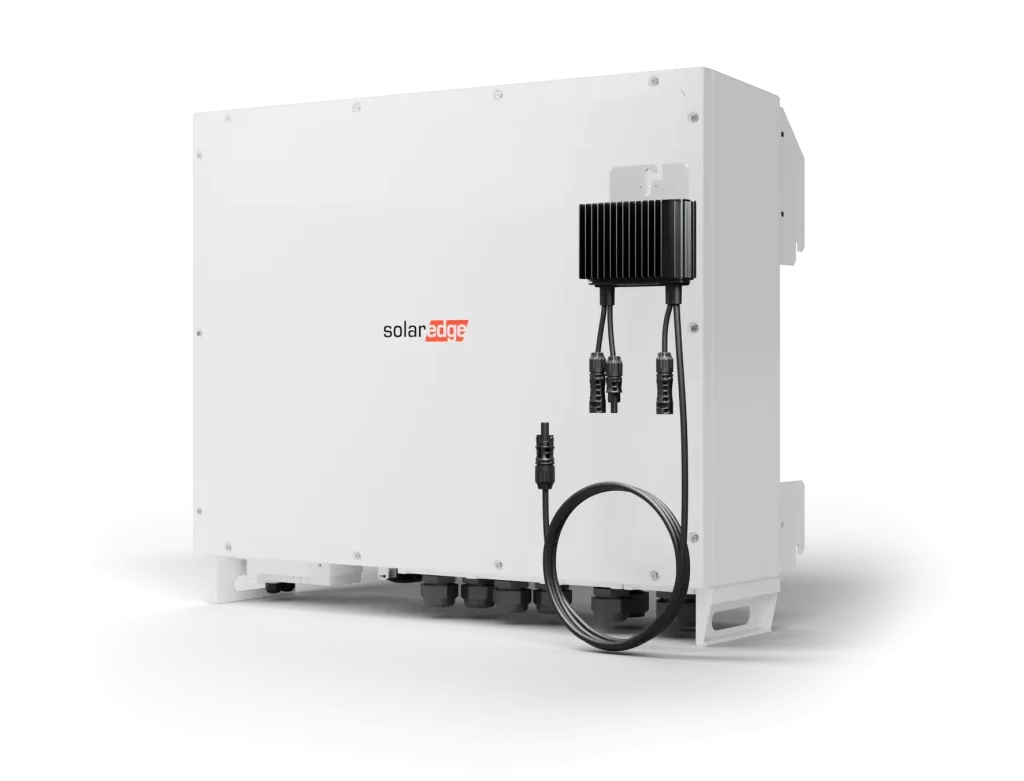 A white SolarEdge inverter with connectors attached is displayed against a black background. The SolarEdge logo is prominently visible on the front of the inverter. The device has a sleek rectangular design and is elevated slightly from the surface it sits on.